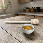 Honey dipper and small bowl of honey on a wooden table in a kitchen setting