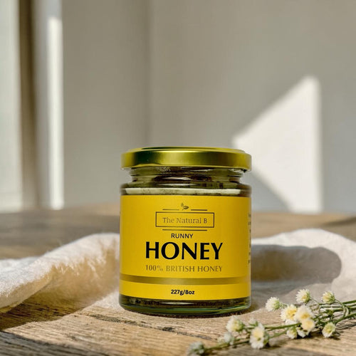 Jar of honey with a yellow label on a wooden surface with flowers