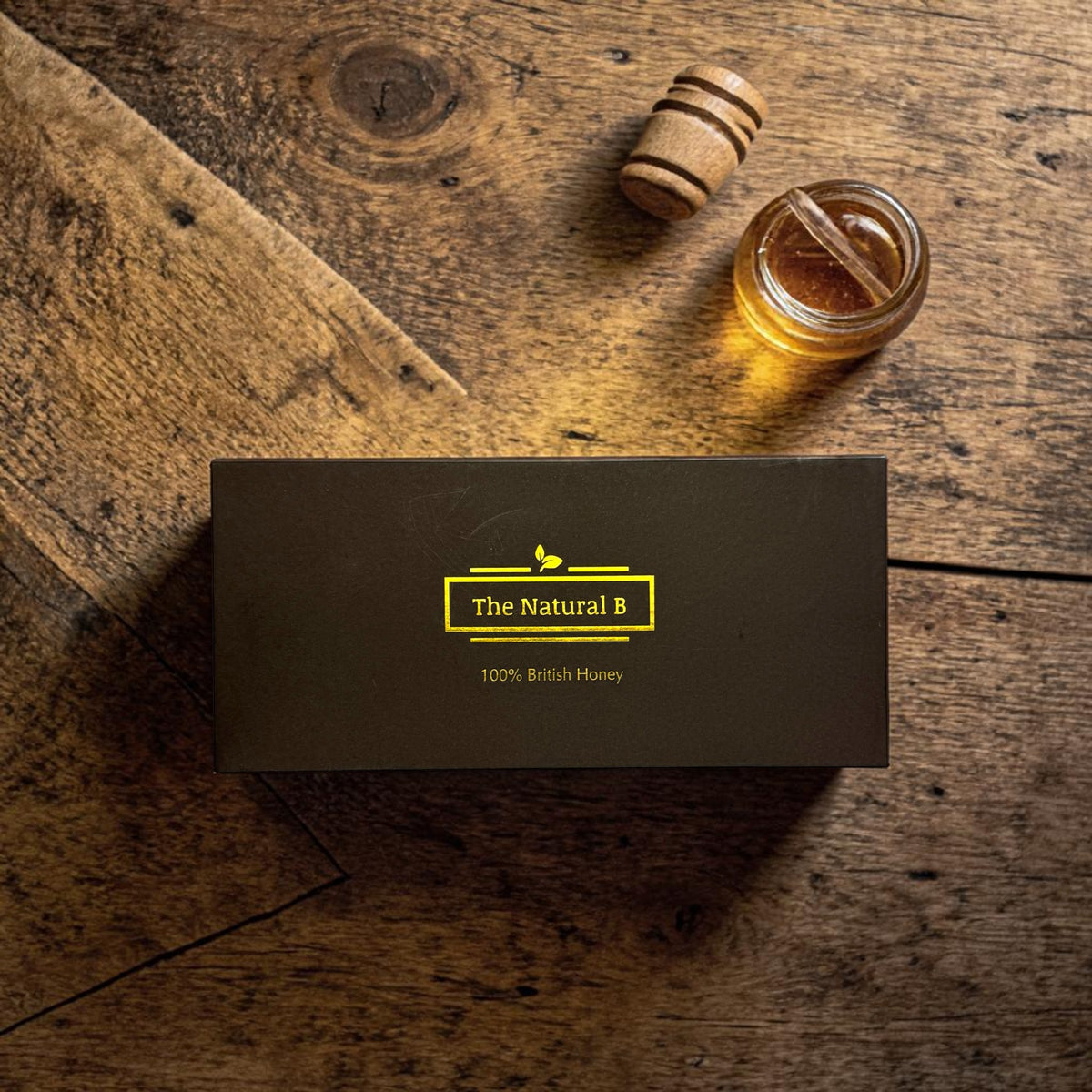 Honey jar and honey dipper on a wooden surface with 'The Natural B' branding.