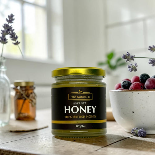 Jar of honey with a black label on a wooden table with lavender and berries in the background