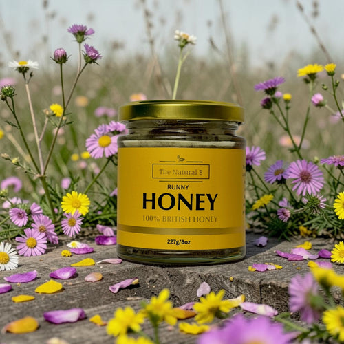 Jar of honey with a yellow label surrounded by flowers on a wooden surface