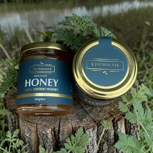 Two jars of Heather Honey by The Natural B on a wooden surface with a natural background