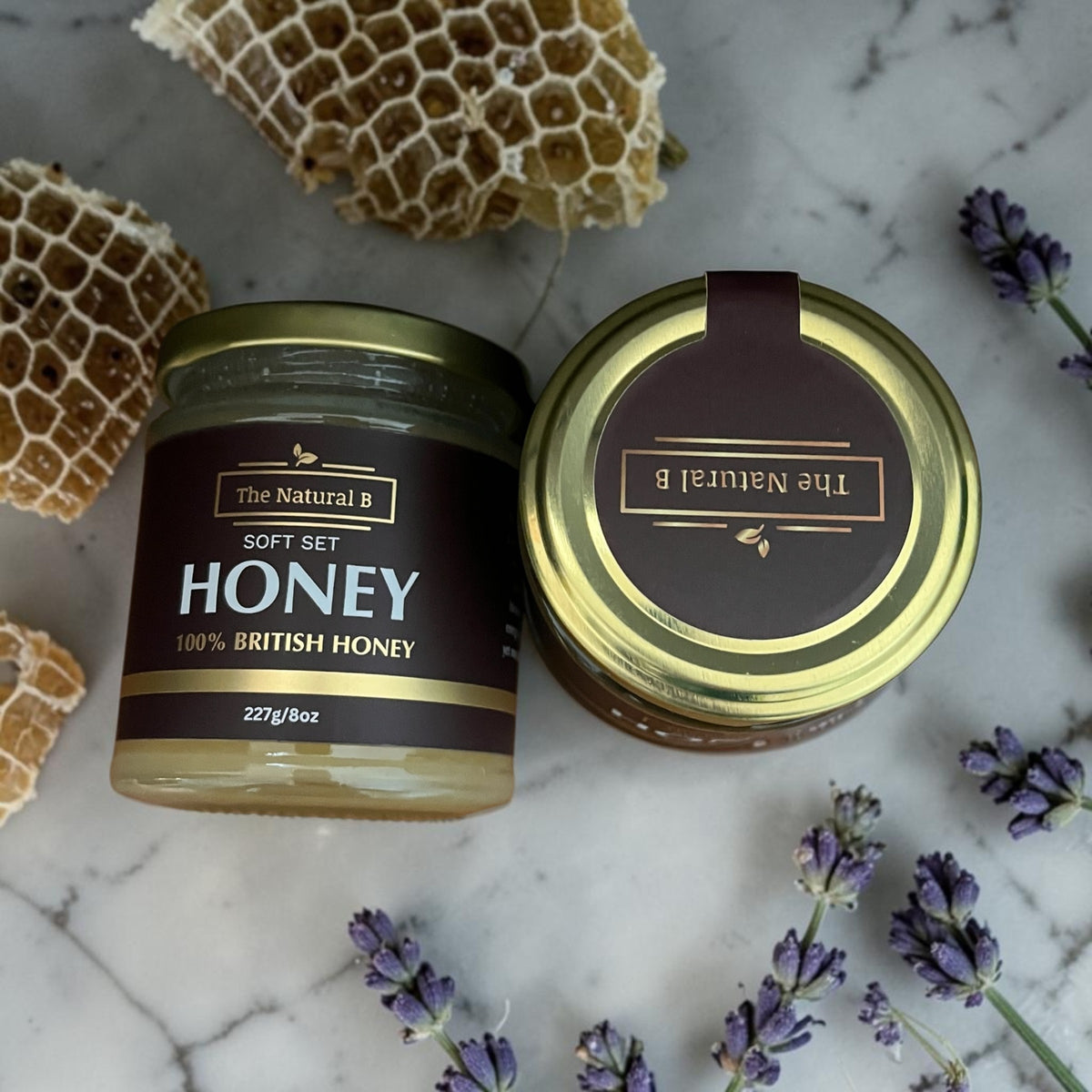 Two jars of honey with honeycomb and lavender on a marble surface