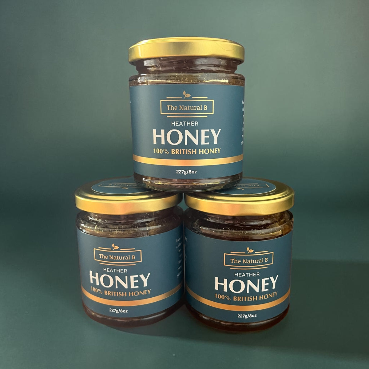 Three jars of 'The Natural B' Heather Honey stacked on a green background