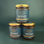 Three jars of 'The Natural B' Heather Honey stacked on a green background