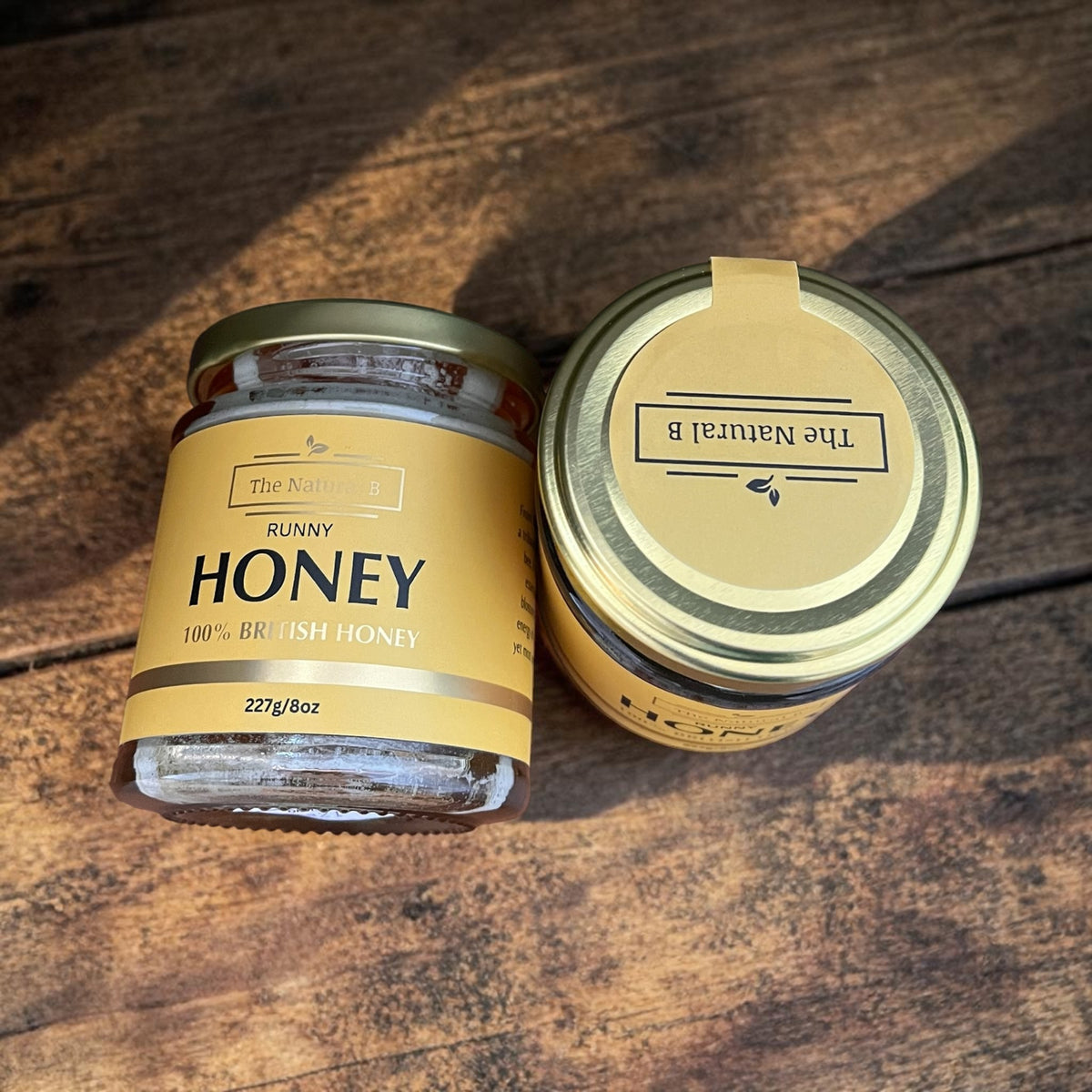 Two jars of honey with gold labels on a wooden surface